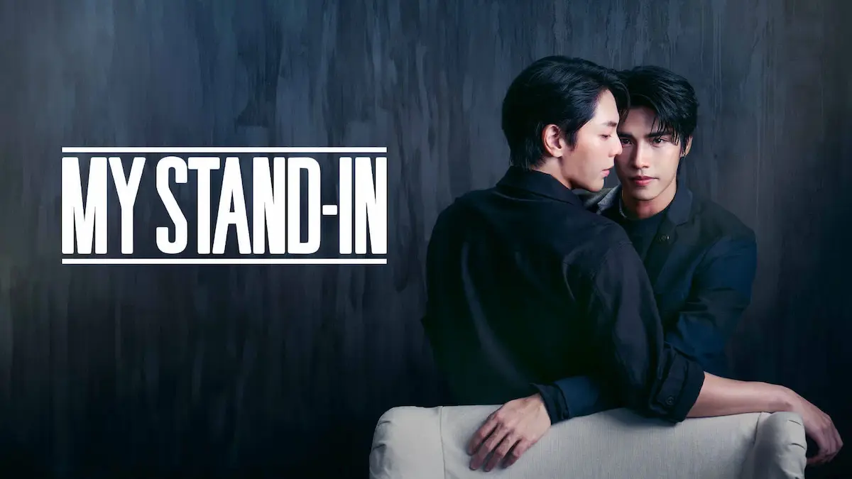 Two men in dark shirts embracing closely near a white chair against a dark grey background